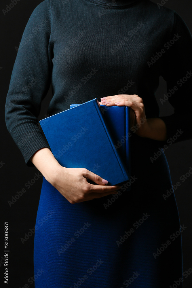 Young woman with blue books on dark background, closeup