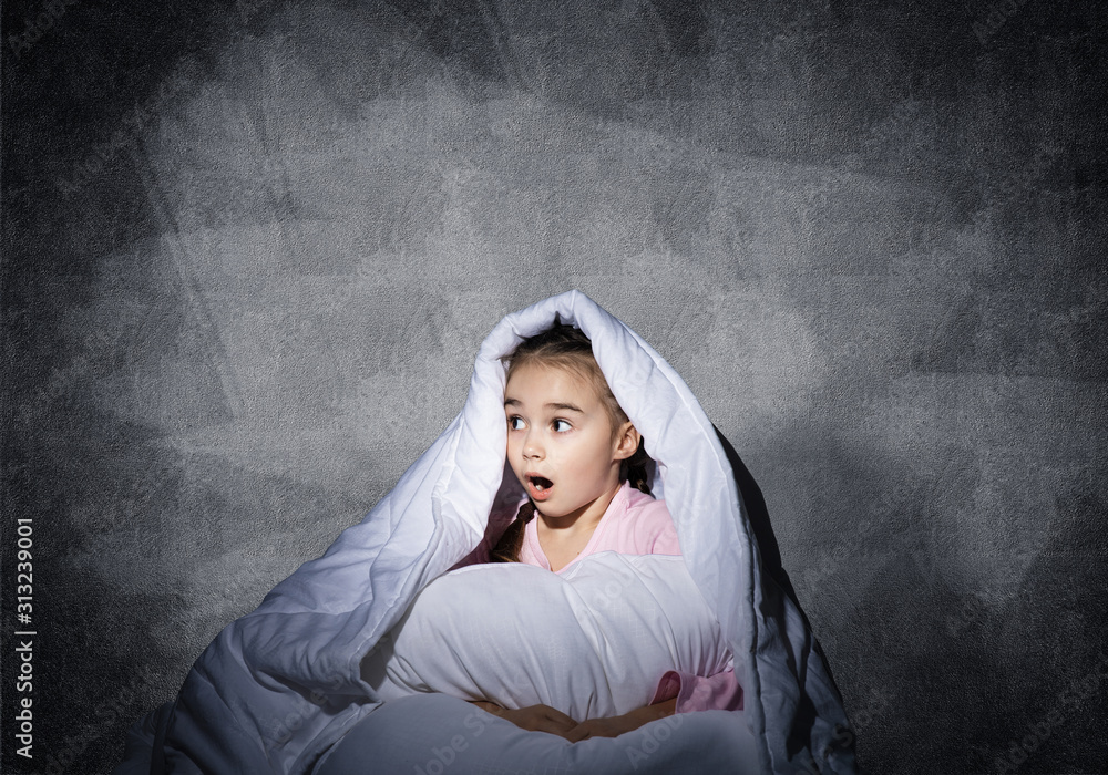 Surprised child hiding under blanket