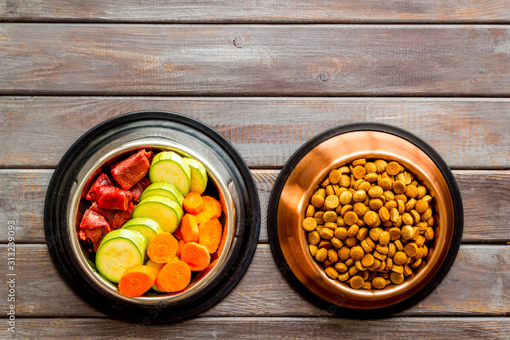 Healthy feed for cats and dogs. Bowls full of dry feed, meat and vegetables on dark wooden backgroun