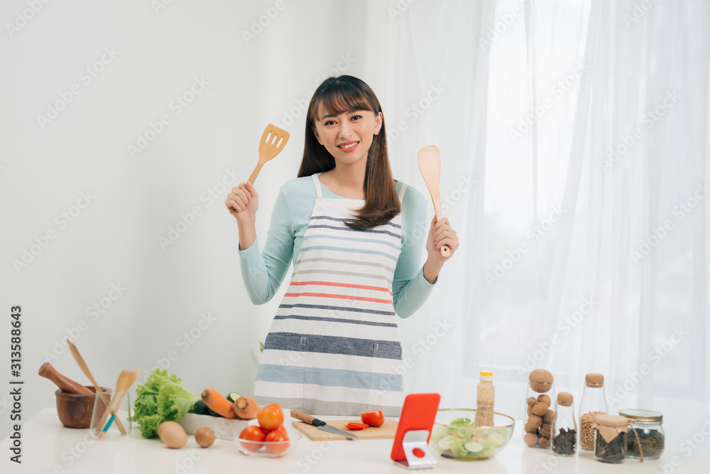 美丽的亚洲年轻女子一边做沙拉一边阅读烹饪食谱或观看节目