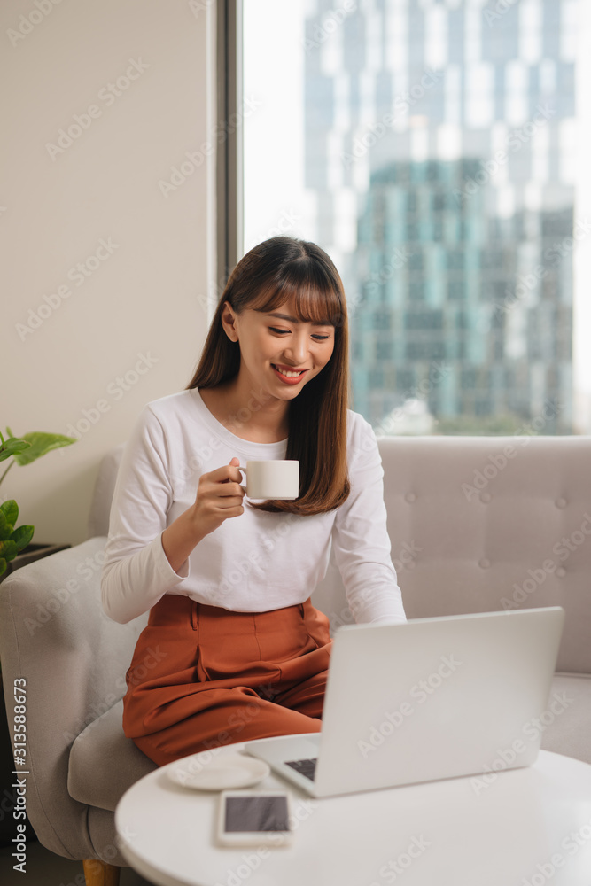 女孩坐在沙发上喝早茶，用笔记本电脑