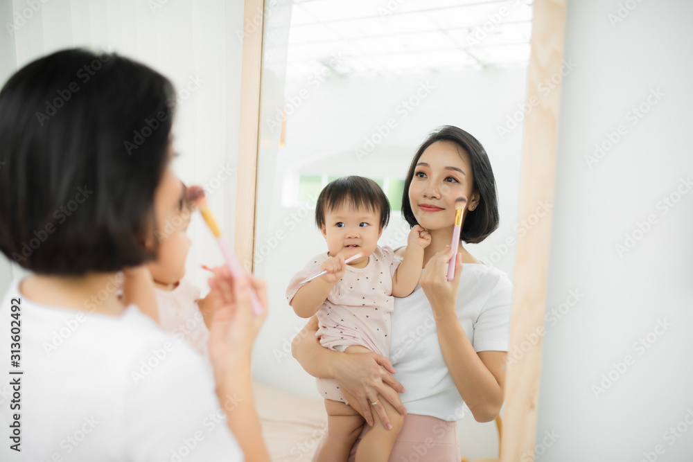 家里有个有趣的家庭。妈妈和她的小女儿正在化妆，在镜子附近玩得很开心。巴