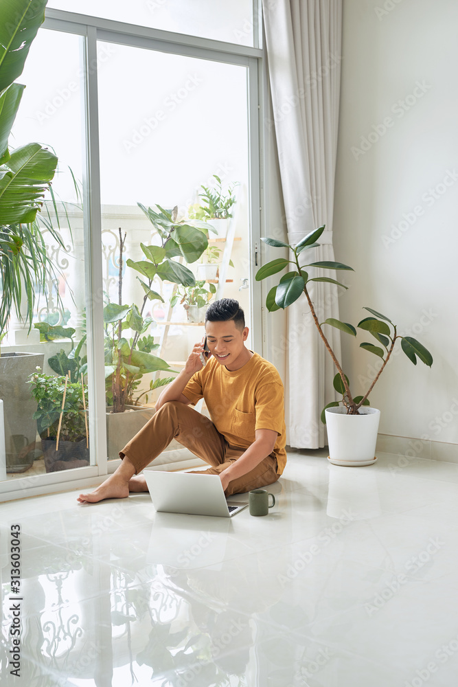 Guy Talking On Cellphone Using Laptop Sitting On Floor At Home