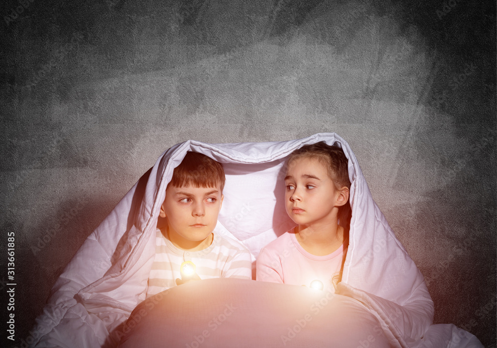 Scared children with flashlights in bed