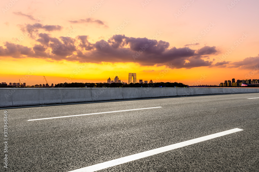 空旷的柏油公路和日落时天空五彩缤纷的苏州城市天际线。