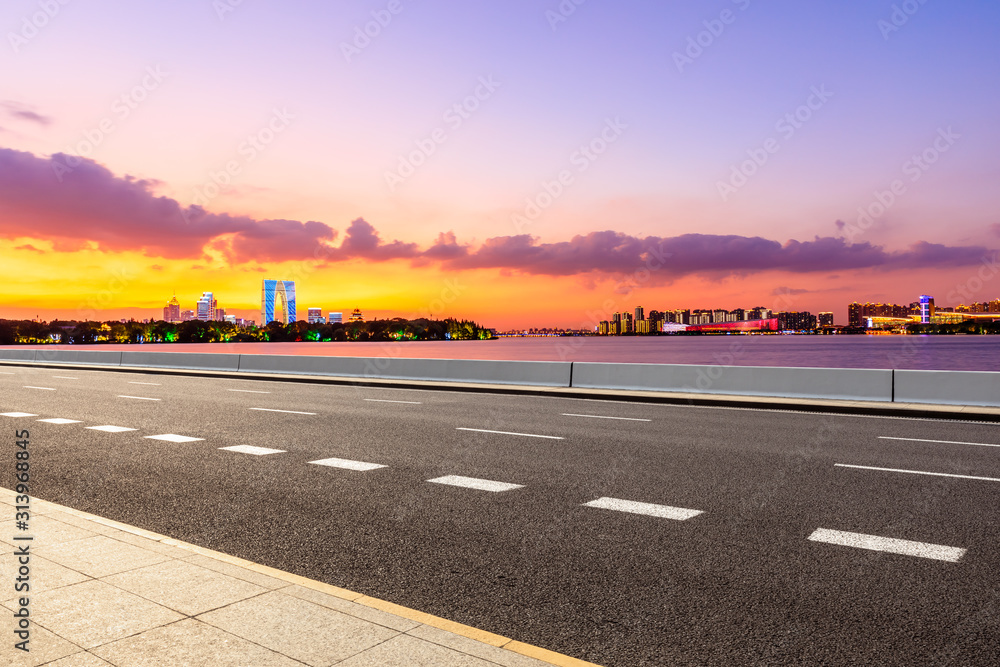 空荡荡的柏油公路和日落时天空色彩斑斓的苏州城市天际线。