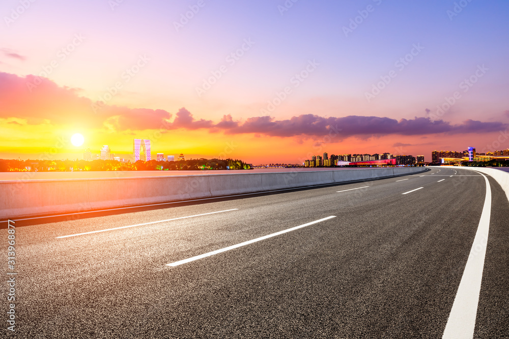 空旷的柏油公路和日落时天空五彩缤纷的苏州城市天际线。