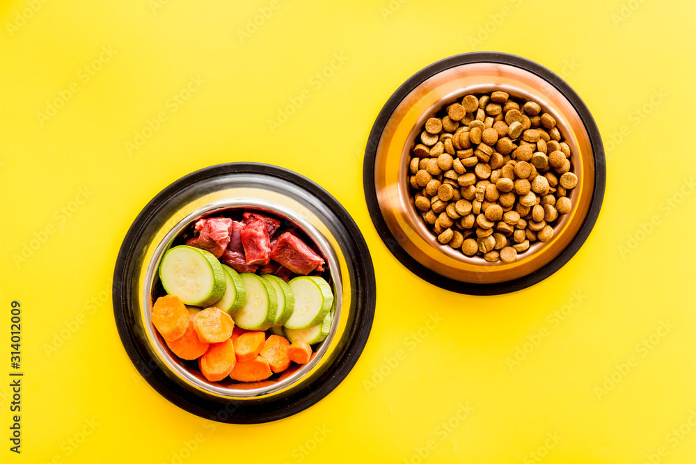 Healthy feed for cats and dogs. Bowls full of dry feed, meat and vegetables on yellow background top