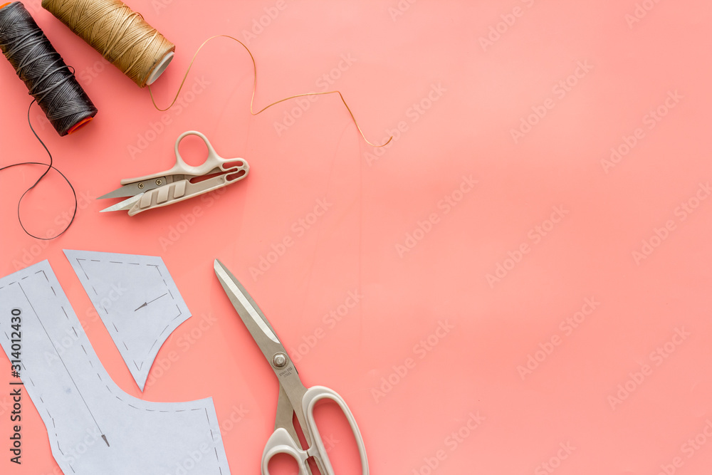 Clothes designer work desk. Pattern, scissors, thread on pink background top-down copy space