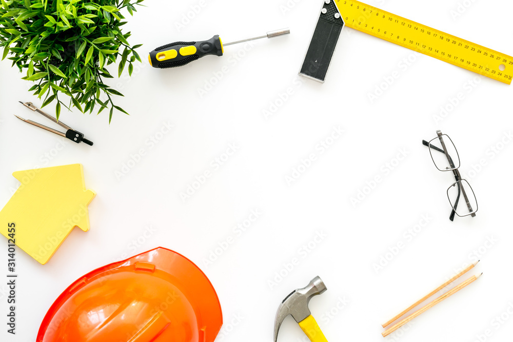 Construction concept. Helmet, tools on work desk, house cutout on white background top-down frame co