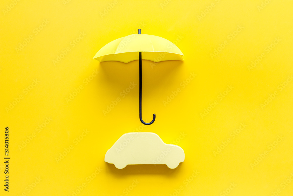 Car insurance. Automobile toy under umbrella on yellow background top-down copy space