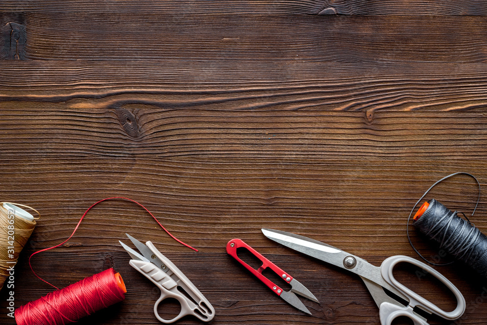 Tailors work desk. Thread and sciccors on dark wooden background top-down copy space