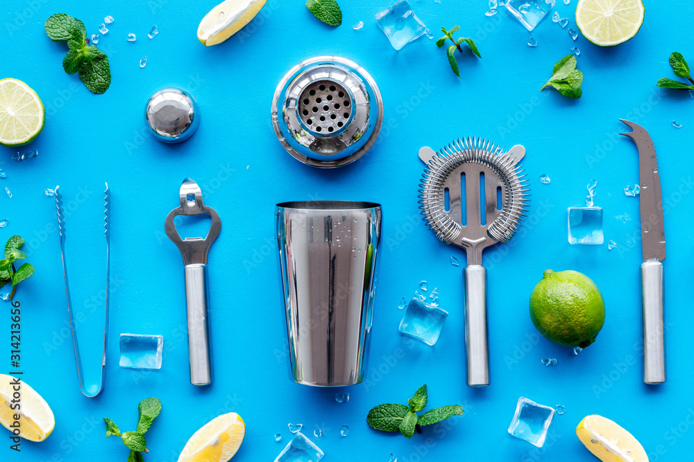 Bartender work desk with equipment and cocktail ingredietns Shaker, lime, ice on blue background top