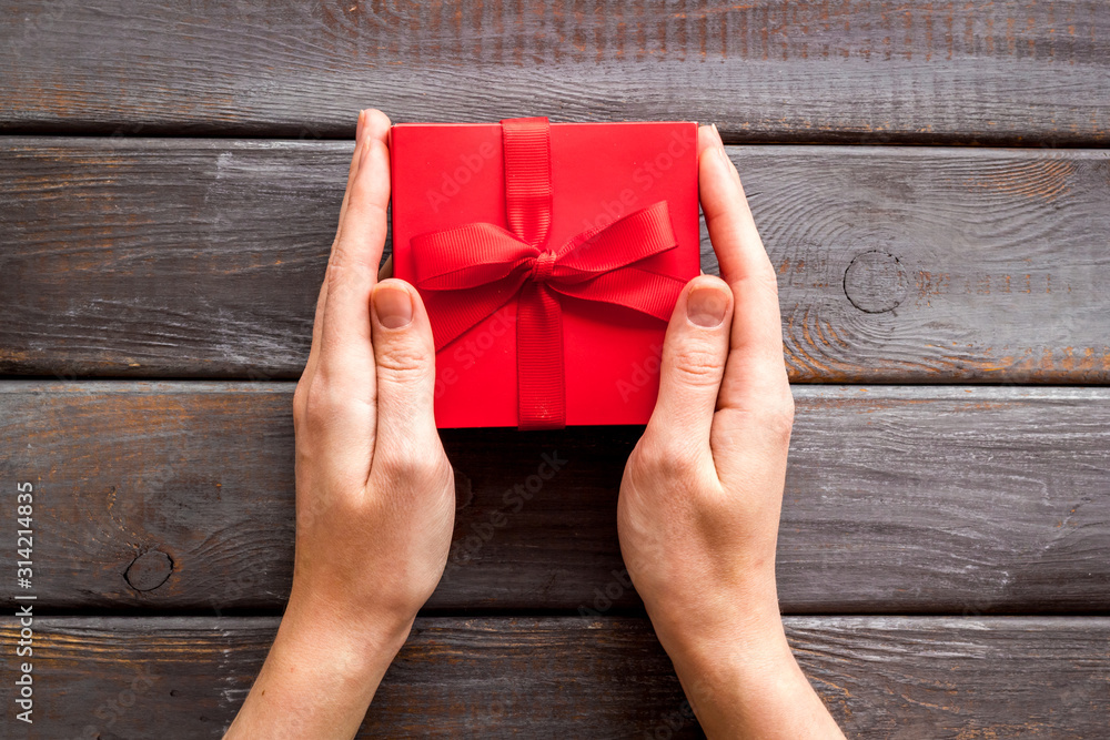 Give a gift on Valentines Day. Women hand hold beautiful red present box on dark wooden background 