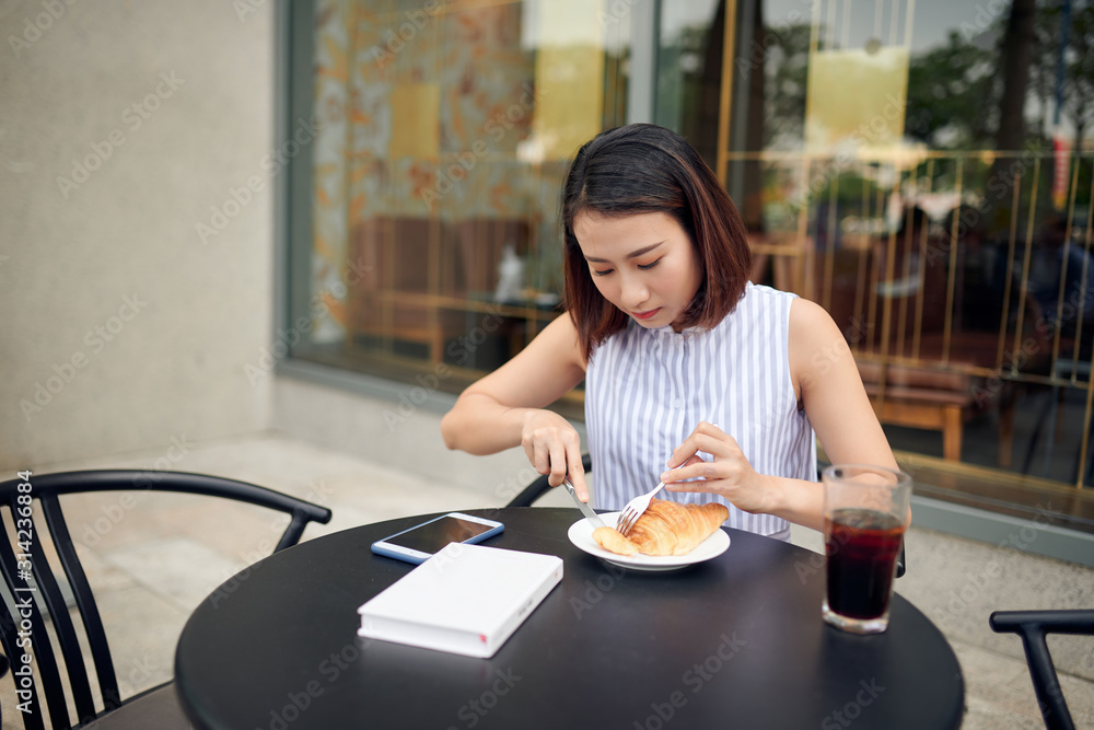 年轻的女人早上坐在桌子旁喝咖啡