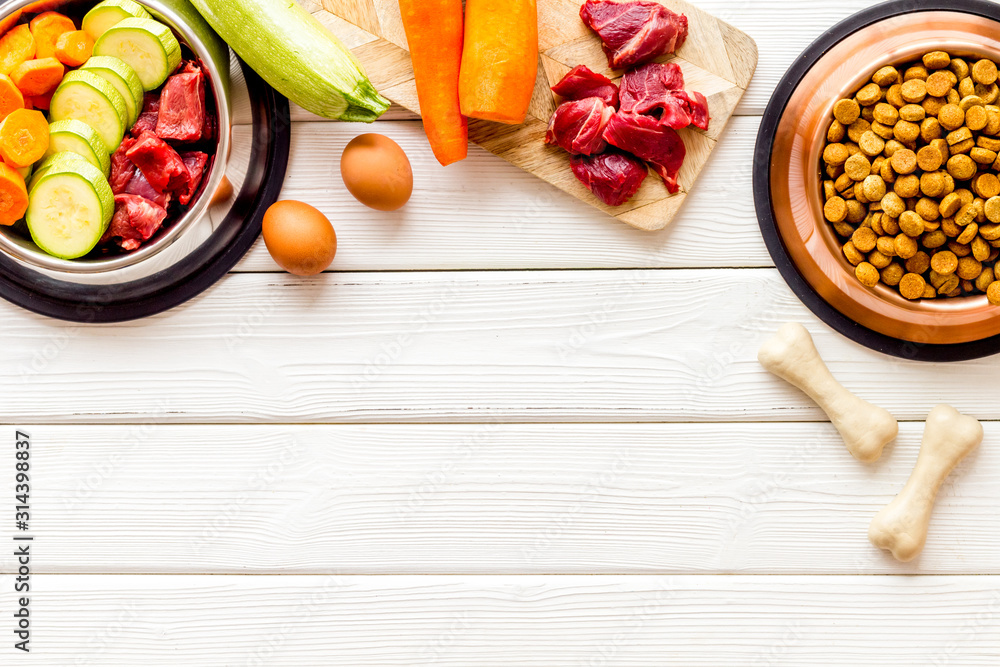 Ingredients of dry feed for dogs - meat, vegetables - near bones on white wooden background top-down