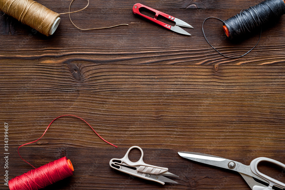 Tailors work desk. Thread and sciccors on dark wooden background top-down copy space