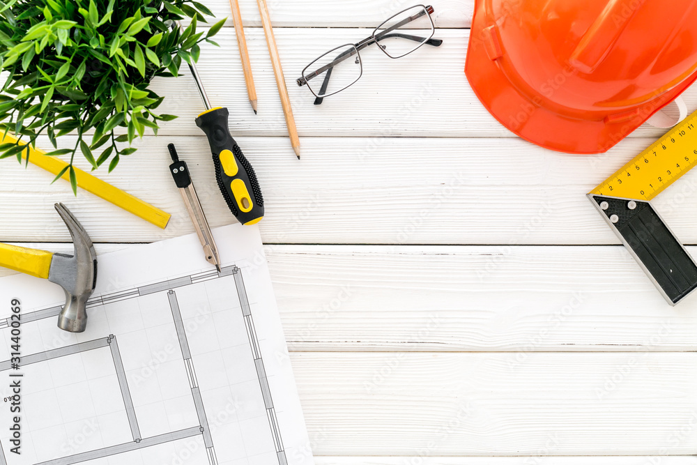 Builder work desk with hard hat, instruments and blueprints on white wooden background top-down fram