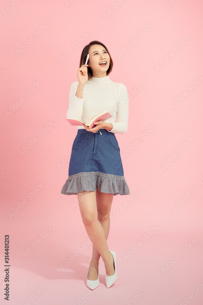 Full length portrait of a smiling beautiful woman holding isolated on a pink background.