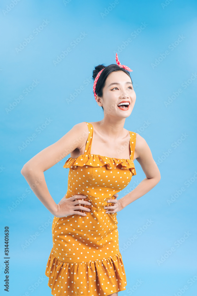 Attractive woman posing in polka-dot dress standing on blue background. Pin-up style.