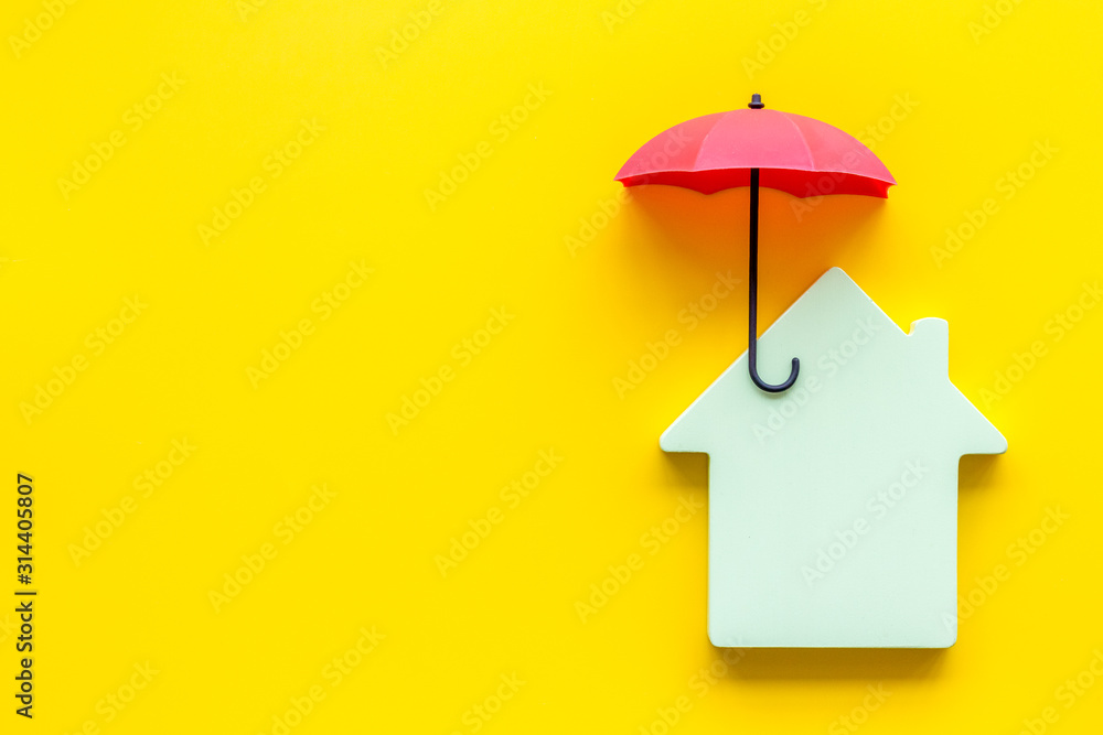 House insurance concept. Toy house defended by umbrella on yellow backgound top view copy space