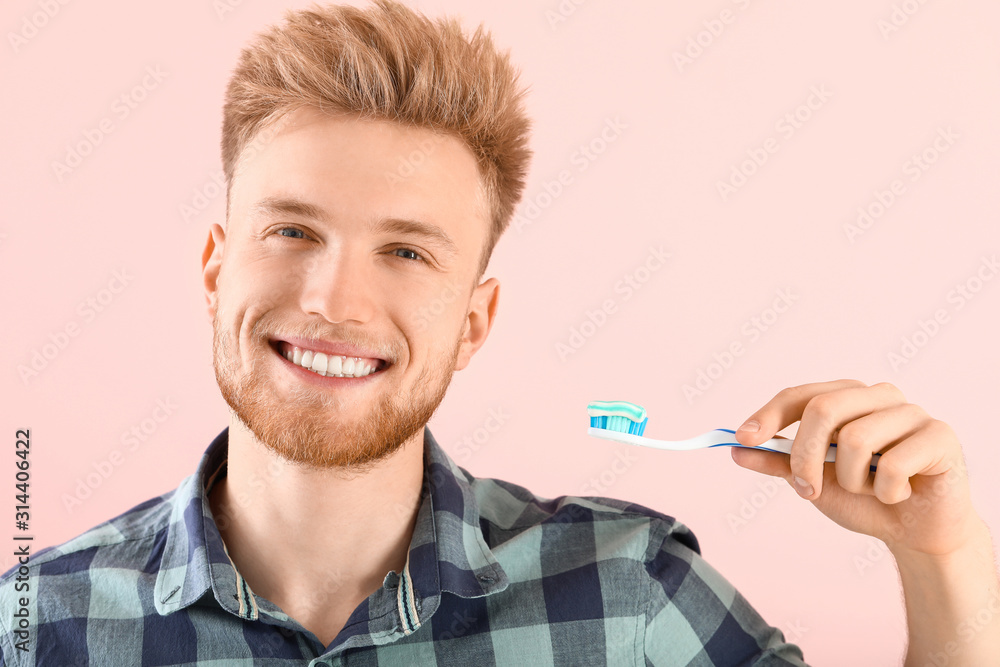 Young man brushing teeth on color background