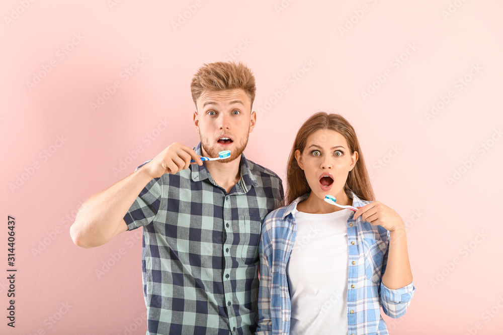 Shocked young couple brushing teeth on color background