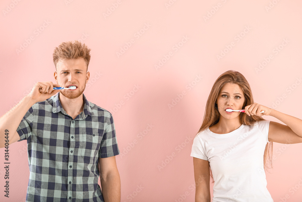 Young couple brushing teeth on color background