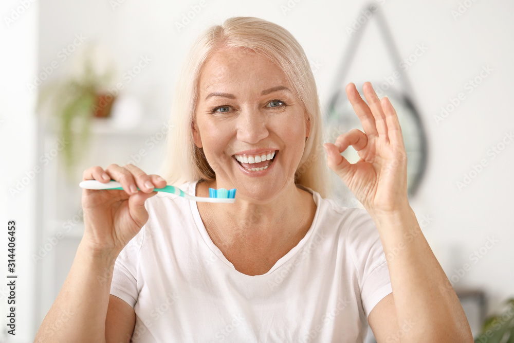 Mature woman brushing teeth at home