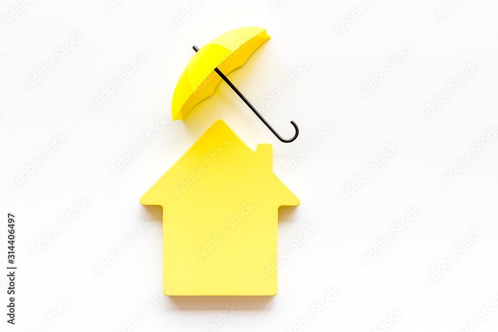 House insurance concept. Toy house defended by umbrella on white backgound top view copy space