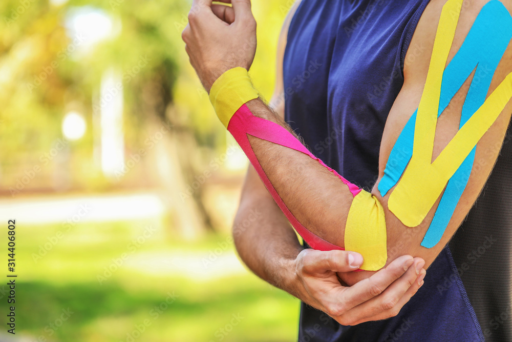 Sporty man with physio tape applied on arm outdoors, closeup