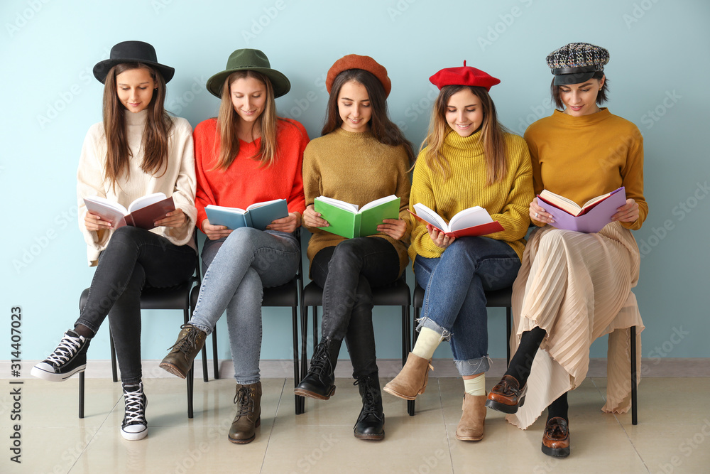 Young women with books sitting near color wall