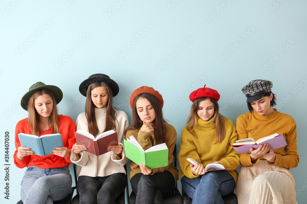 Young women with books sitting near color wall