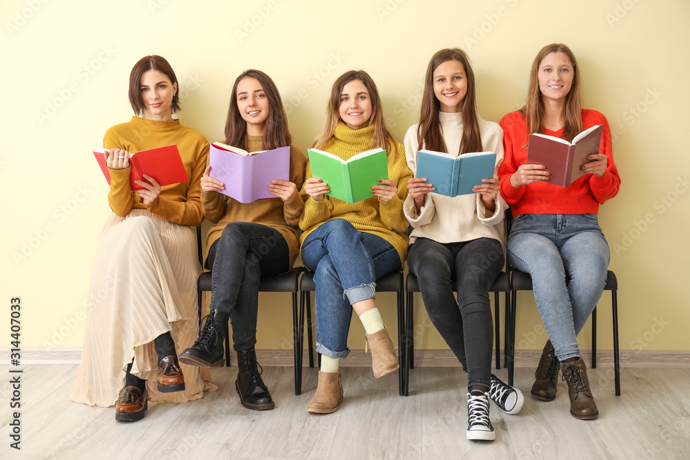 Young women with books sitting near color wall