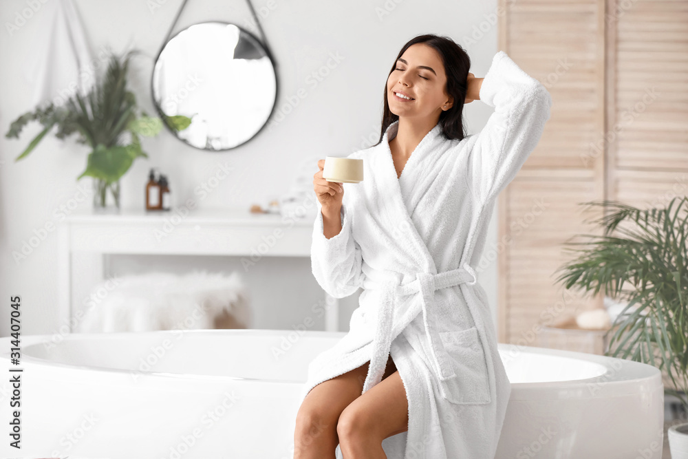 Beautiful young woman drinking coffee in bathroom