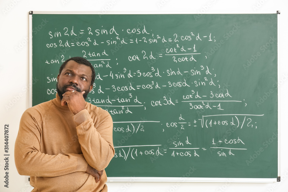 Thoughtful African-American math teacher near blackboard in classroom