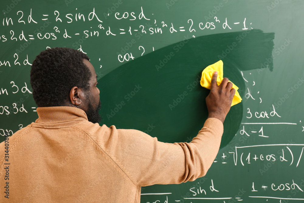 African-American math teacher wiping blackboard in classroom