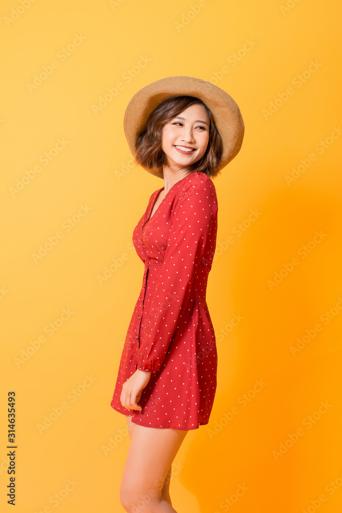 Studio shot of happy energetic asian woman wearing red dress and straw hat over orange background