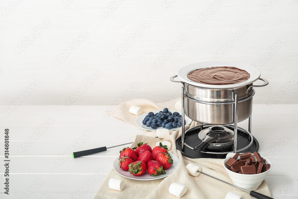 Fondue pot with melted chocolate and berries on table