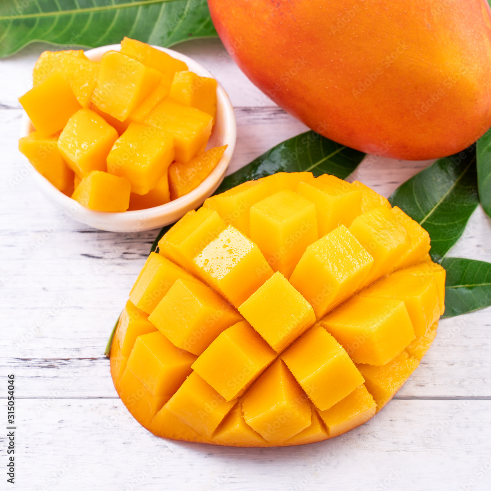 Fresh mango,beautiful chopped fruit with green leaves on bright wooden table background. Tropical fr