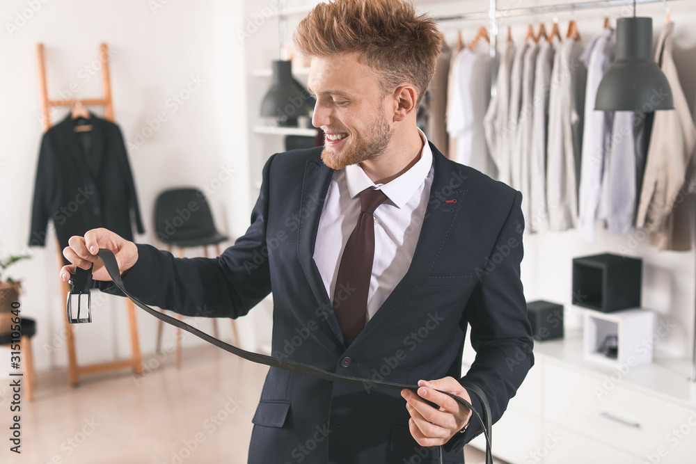 Handsome man choosing belt in dressing room