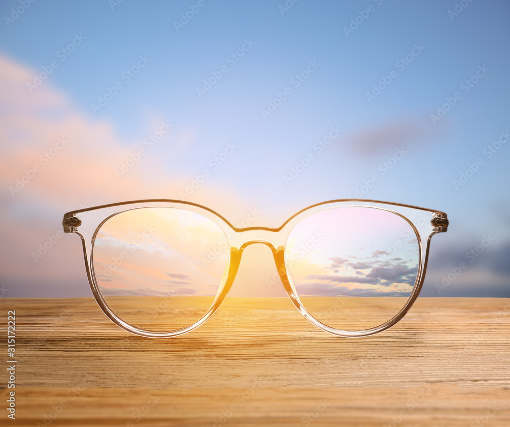 Stylish eyeglasses on wooden table against blue sky