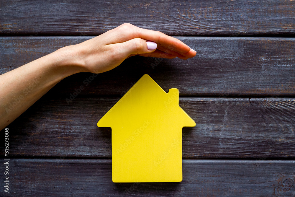 Property insurance concept. Hand defends house cutout on dark wooden backgound top view copy space