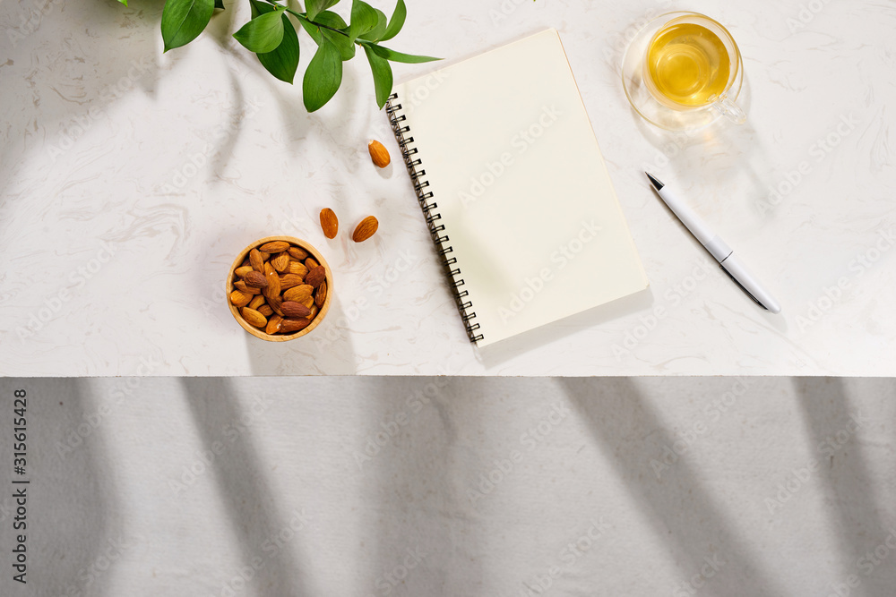 Flatlay of notebook, cake macaron, cup of tea and leaves on white table