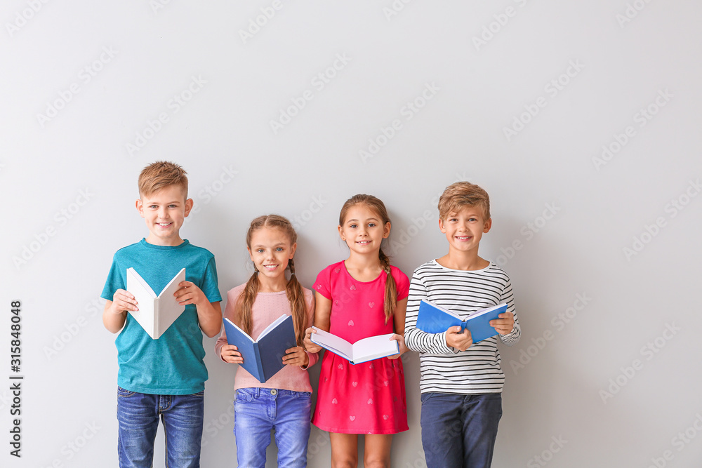 Cute little children reading books on grey background