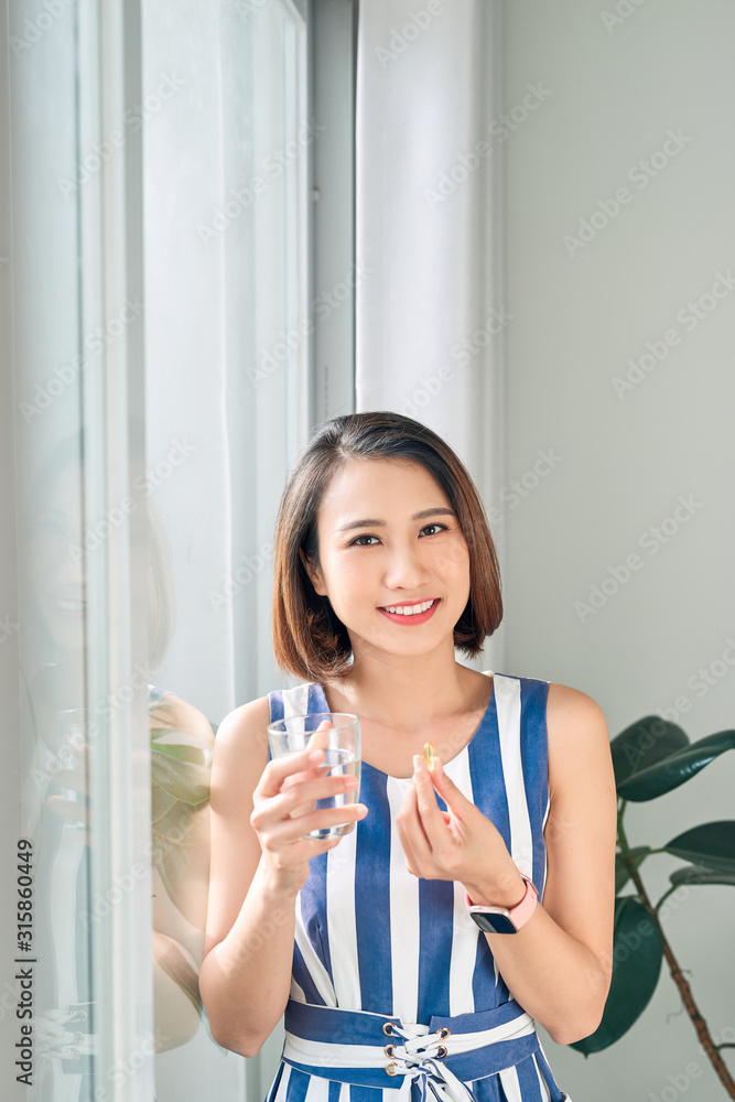 手持水杯和药物/维生素饮料的美丽亚洲女性肖像