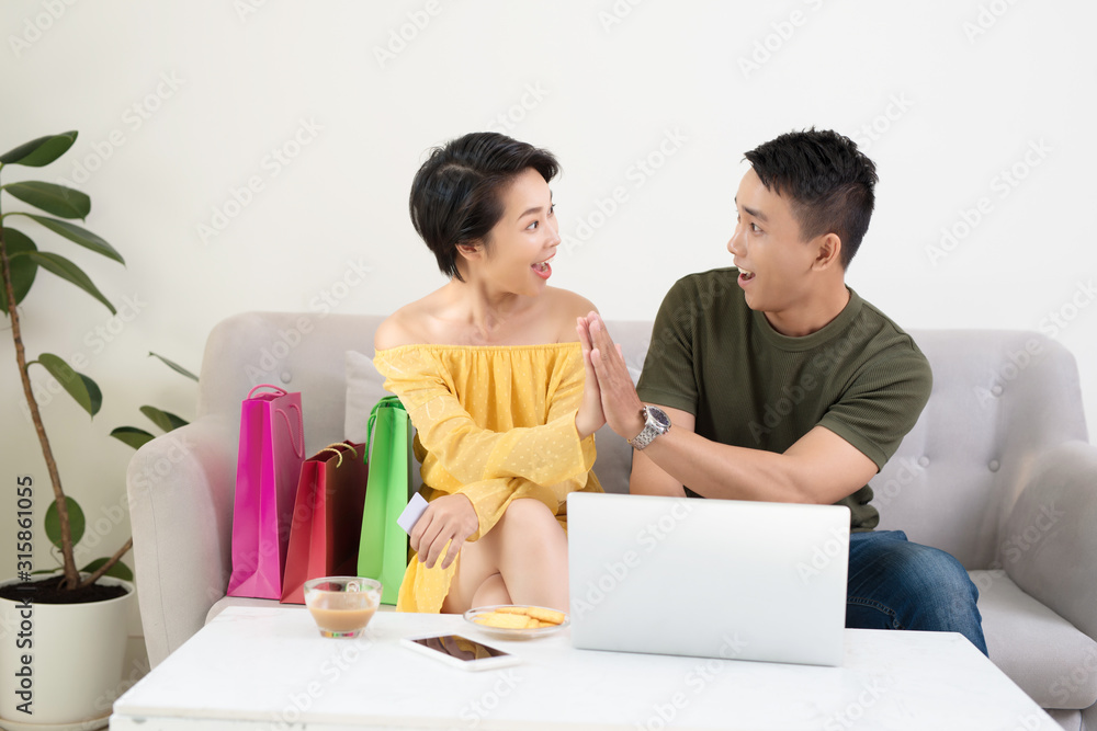 Young Asian couple shopping online on laptop, sitting at home with colorful bags