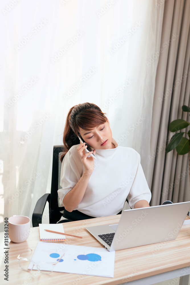 Asian Woman working on laptop at office while talking on phone