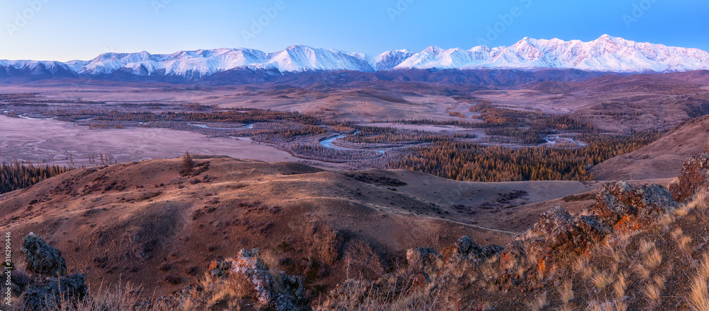 Panorama of snow peaks at dawn view from the hill to the river valley below.