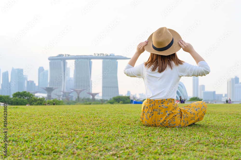 新加坡度假时，一名年轻的亚洲女子坐在滨海公园，背景是滨海湾